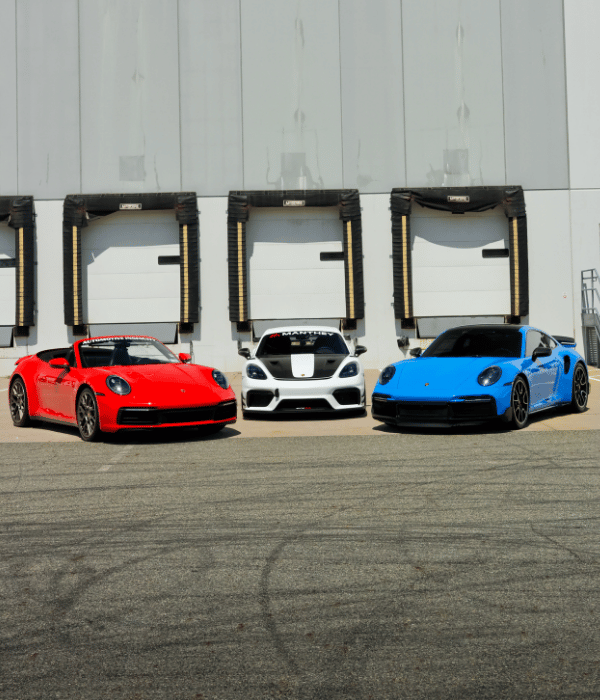 Red and blue Porsche sports cars displayed alongside a white performance vehicle.