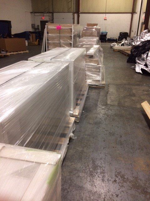 Warehouse floor with shrink-wrapped pallets and long metal equipment on dollies.