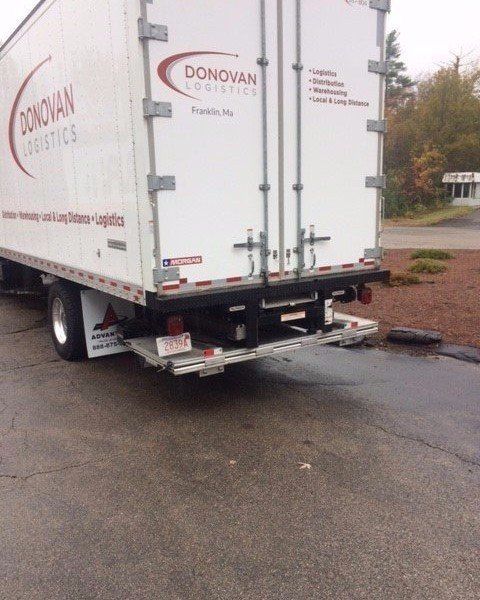 White Donovan box truck parked on a wet road near a curb, rear view.