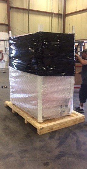 Shrink-wrapped pallet of stacked boxes in a warehouse, with black wrap on top and white wrap below.