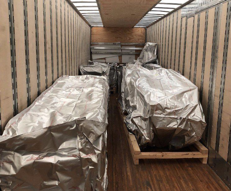 Cargo truck interior loaded with large items wrapped in silver tarps on wooden pallets