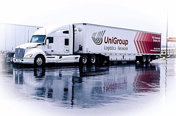 White UniGroup moving truck parked on a wet lot, reflected in the pavement.