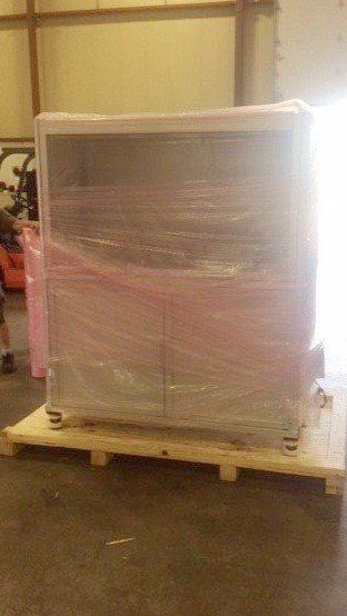 Shrink-wrapped cabinet on a wooden pallet in a warehouse or storage area.