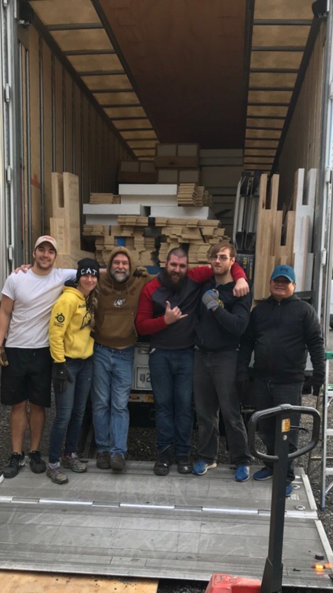 Group of six people standing on a moving truck with furniture and boxes behind them