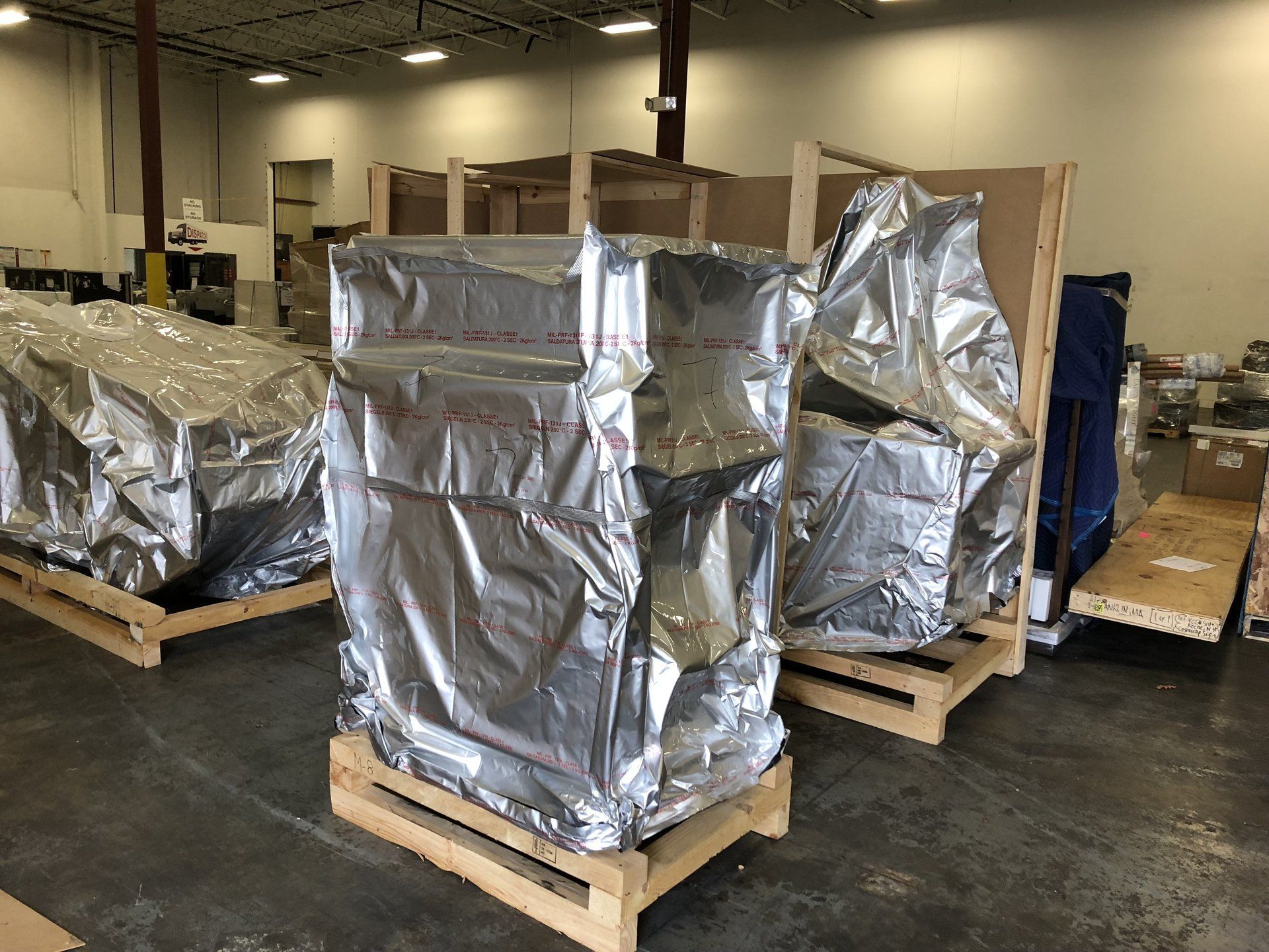 Pallets of large equipment wrapped in shiny silver protective foil inside a warehouse