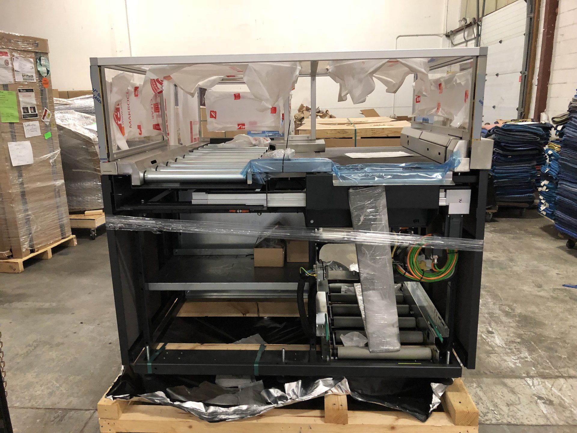 Damaged black metal display cabinet in a warehouse, with broken glass and torn wrapping on top.