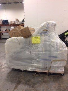 Pallet wrapped in plastic in a warehouse, with cardboard boxes on top and a yellow label attached.