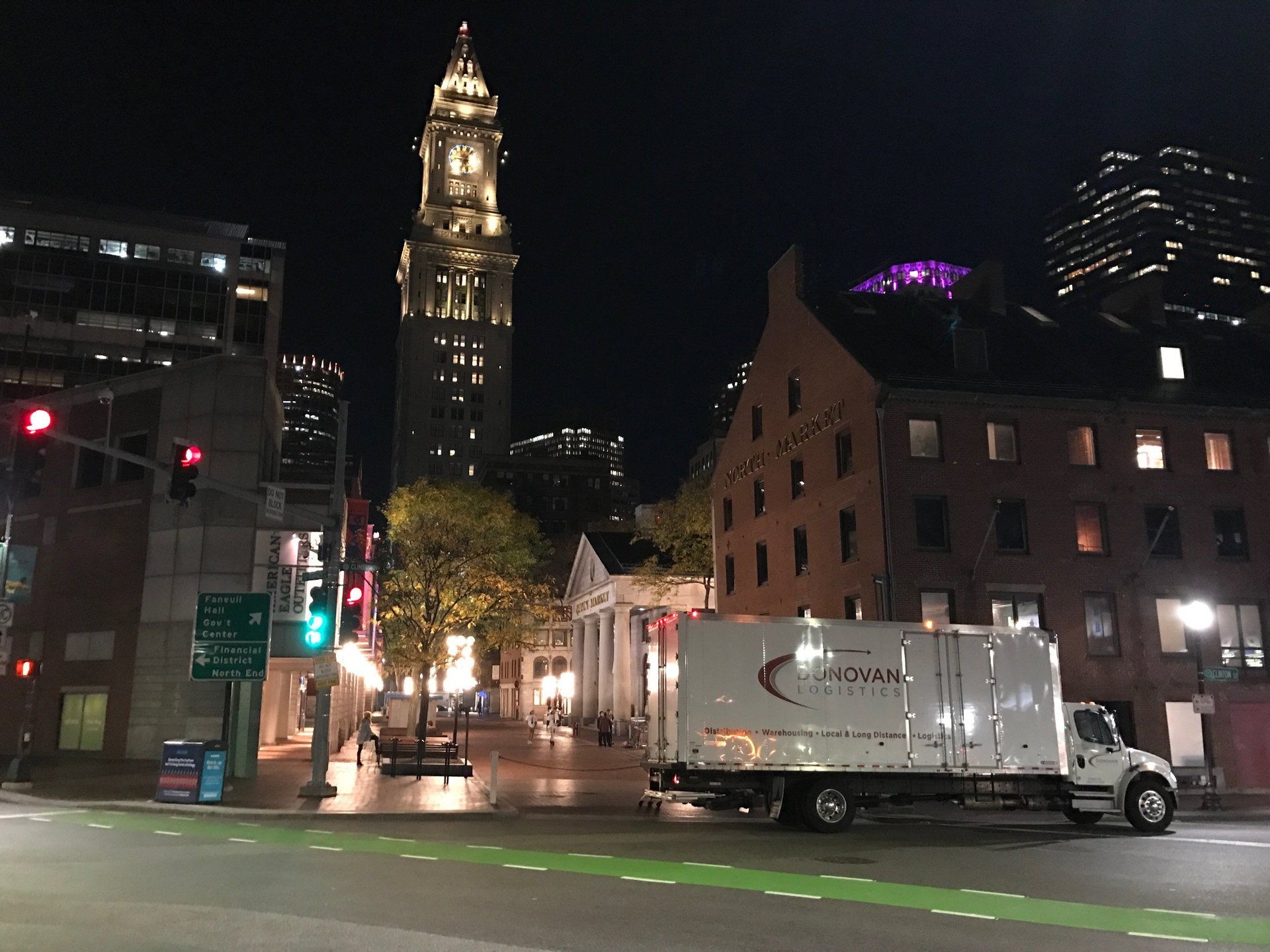 Night city street with lit tower, brick buildings, and a white box truck at an intersection
