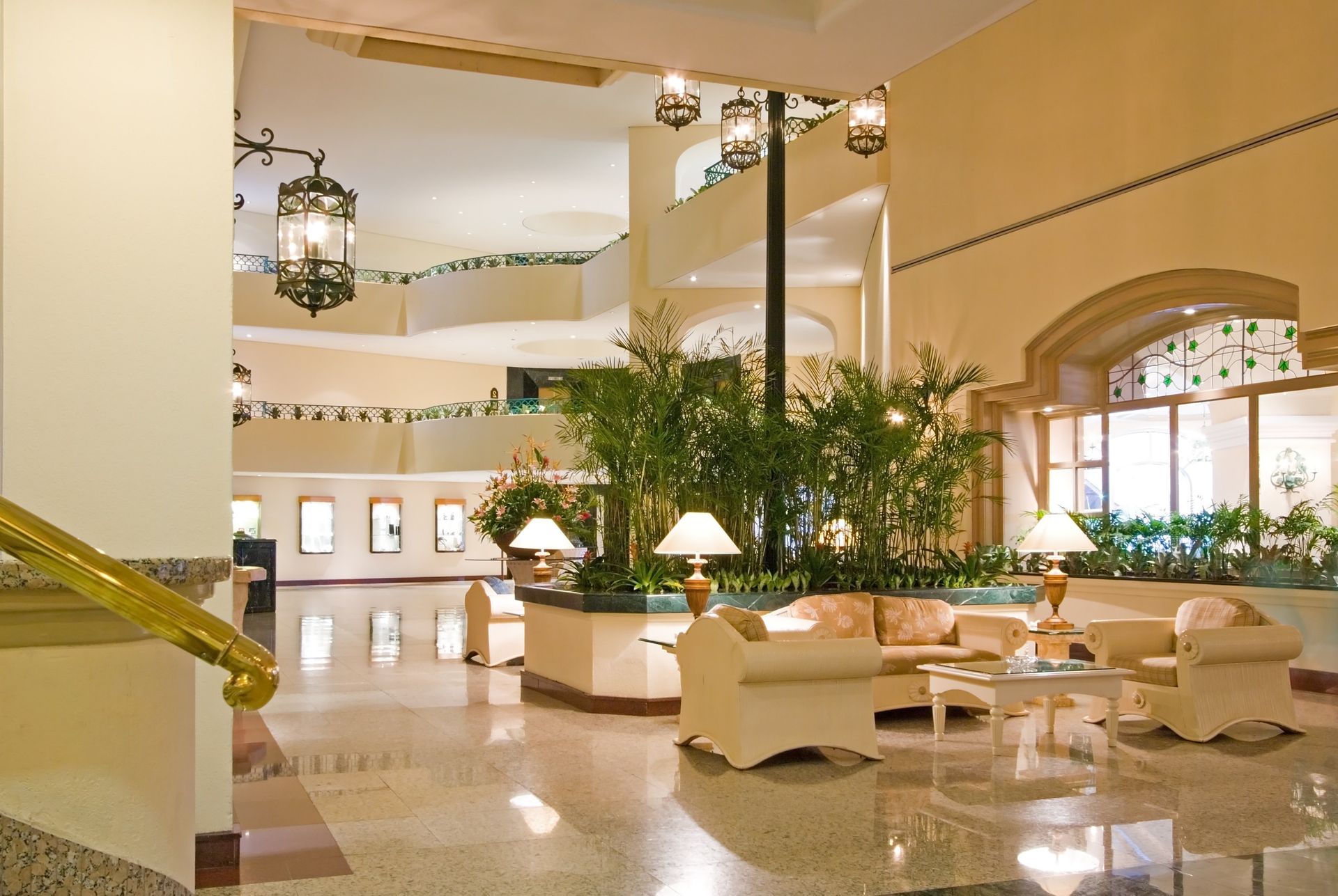 Elegant hotel lobby with cream sofas, tall plants, chandeliers, and polished marble floors