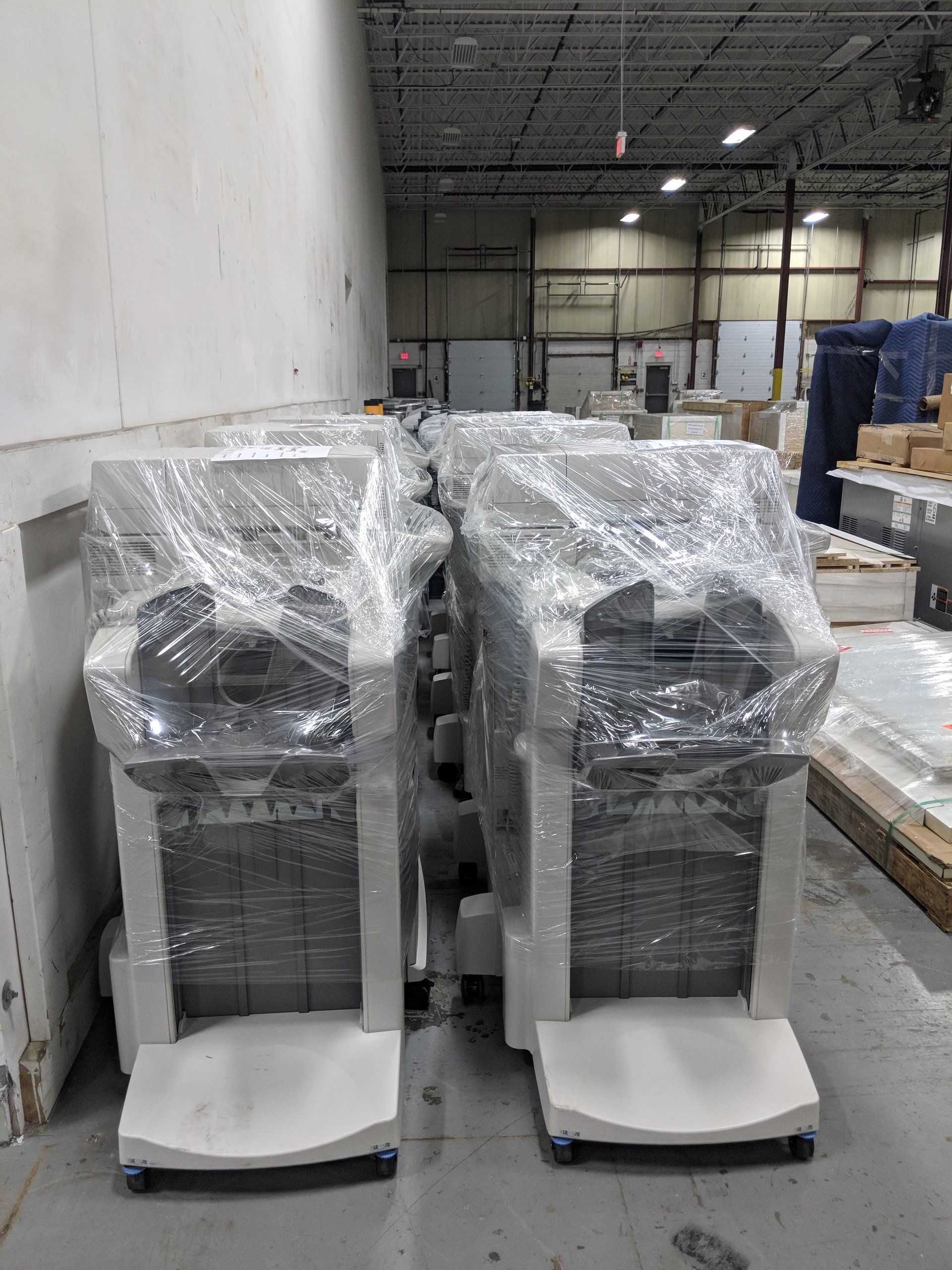 Two shrink-wrapped industrial machines on pallets in a warehouse aisle