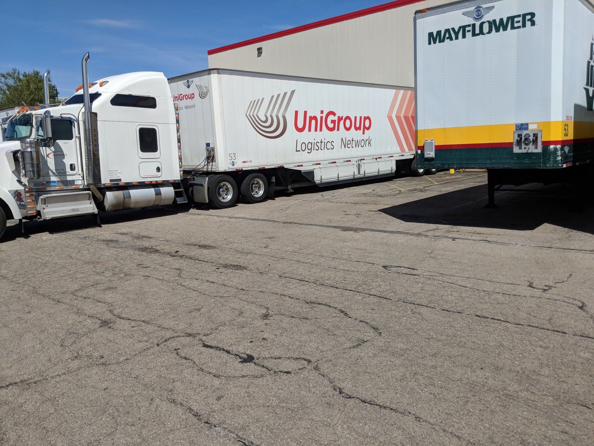 White semi truck with UniGroup trailer parked beside a Mayflower trailer in a lot