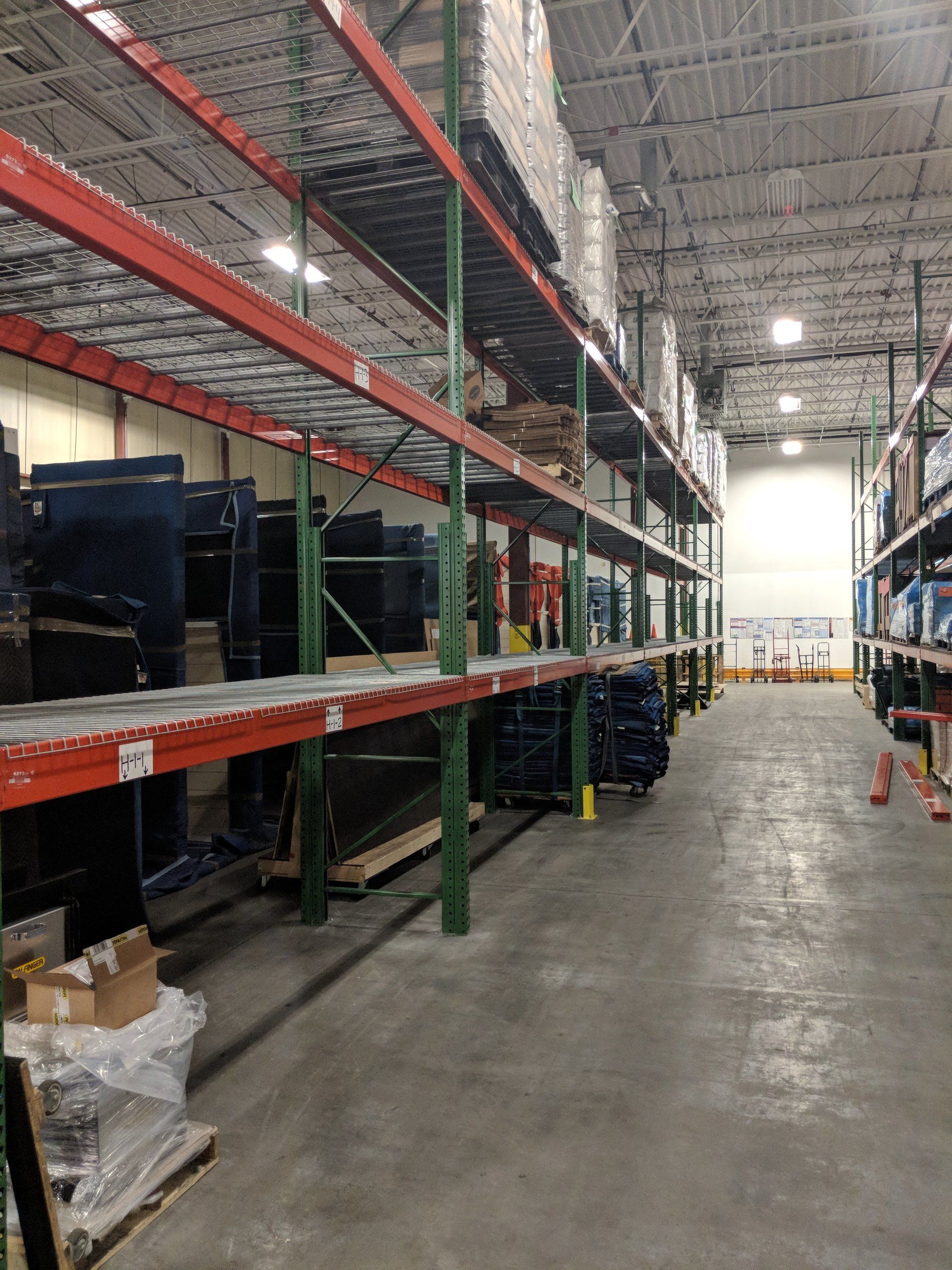Empty warehouse aisle with tall metal shelving and stacked boxes under bright overhead lights