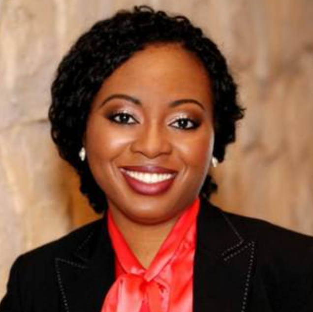 A woman wearing a red shirt and a black jacket smiles for the camera