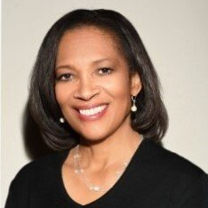 A woman wearing a black shirt and earrings is smiling for the camera.
