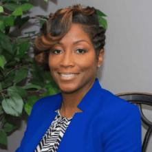 A woman is sitting in a chair wearing a blue jacket and smiling.