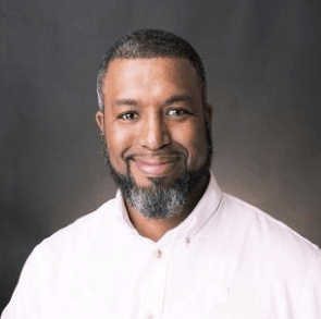 A man with a beard and a white shirt is smiling for the camera.