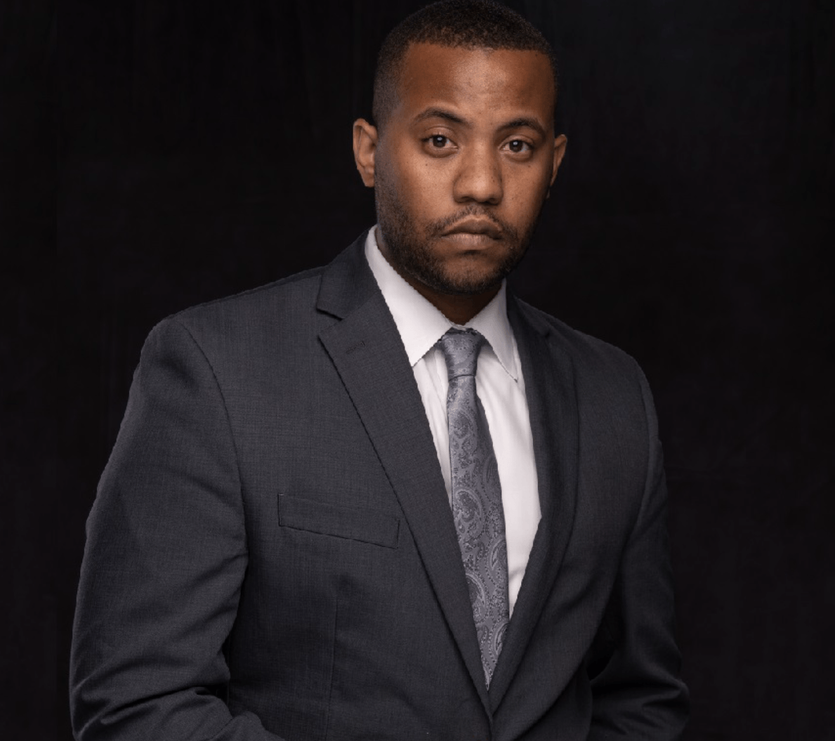 A man in a suit and tie is standing in front of a black background