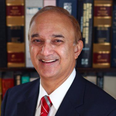 A man in a suit and tie is smiling in front of a bookshelf