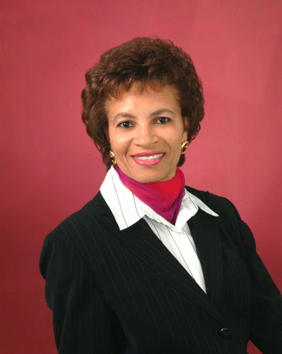 A woman wearing a black suit and a red scarf smiles for the camera