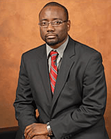 A man in a suit and tie is sitting with his hands folded.