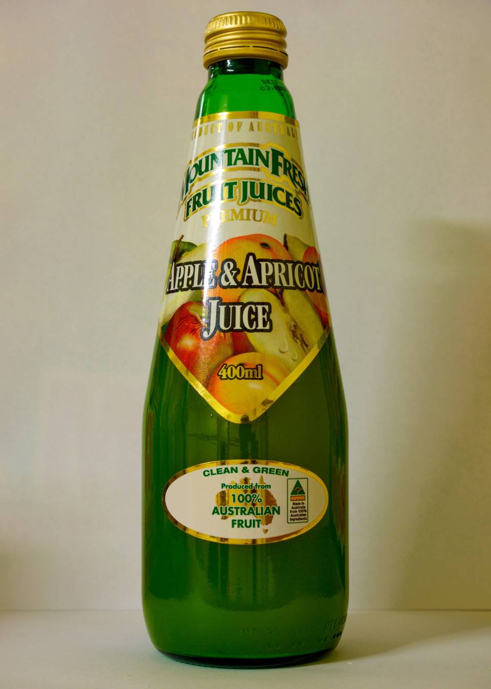 Green glass bottle of apricot juice with a yellow label and gold cap on a plain background