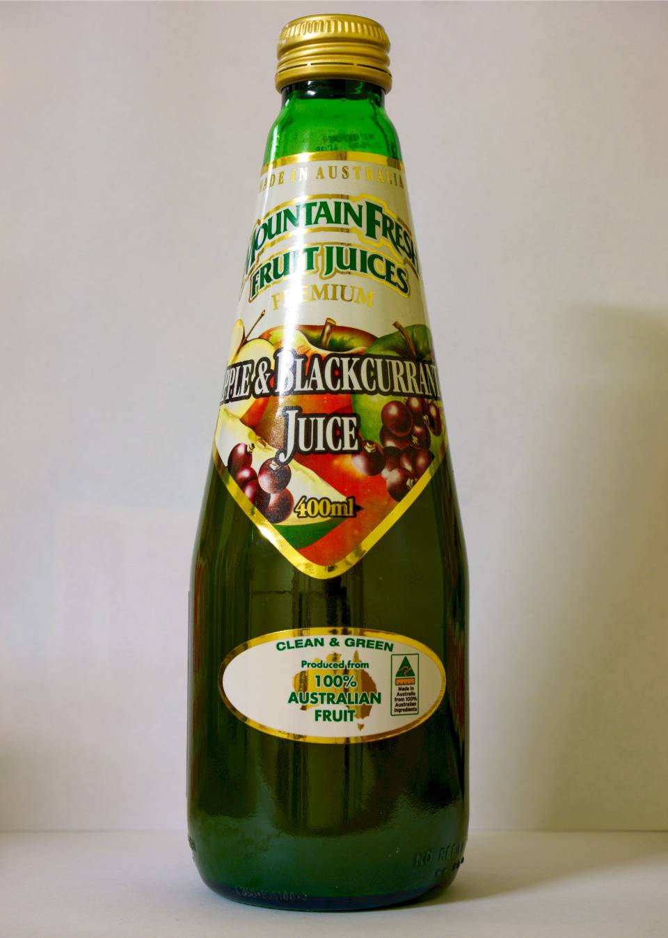 Green bottle of blackcurrant juice with a yellow cap and fruit label on a plain background
