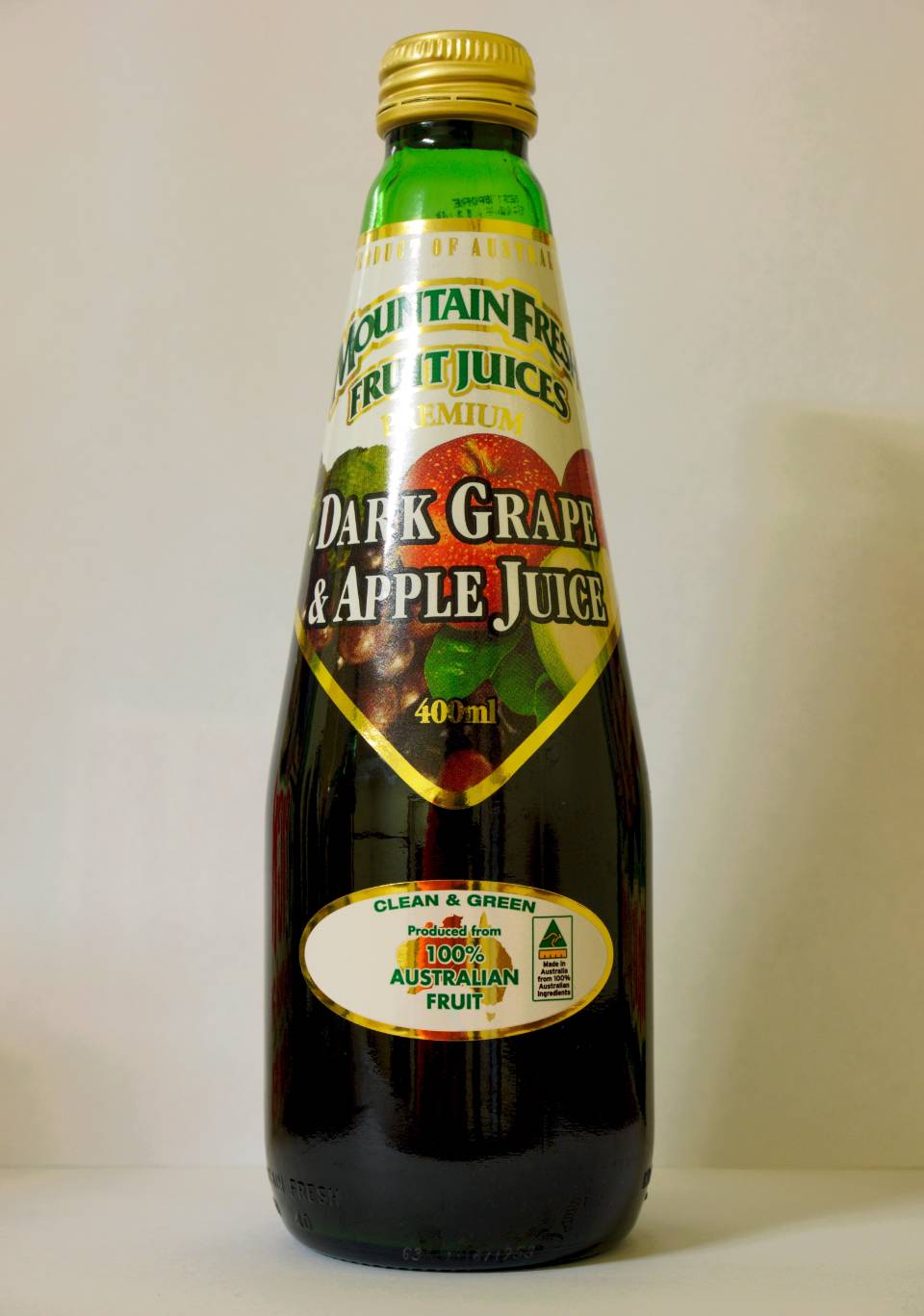 Glass bottle of dark grape apple juice with green label and gold cap on a plain background