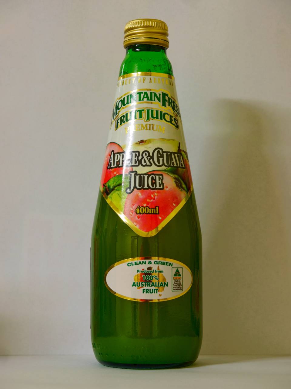 Green glass bottle of orange juice with a gold cap and colorful label against a white background