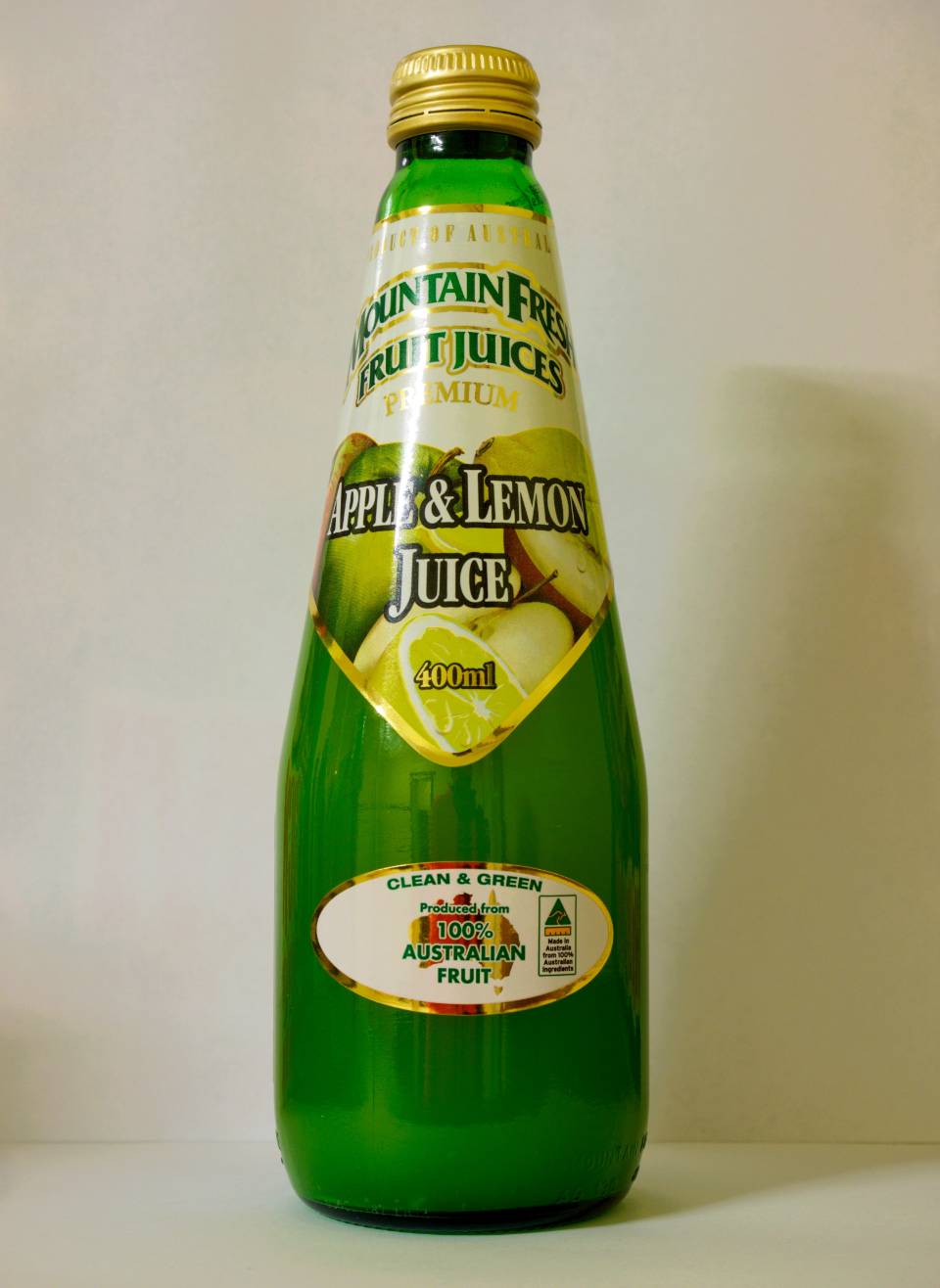 Green glass bottle of Mountain Valley Apple & Lemon Juice with a gold cap on a plain background