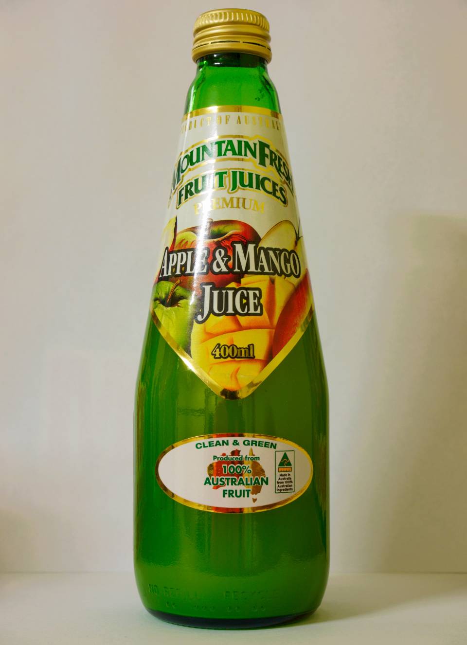 Green glass bottle labeled “Apple & Mango Juice” with a yellow cap on a plain background