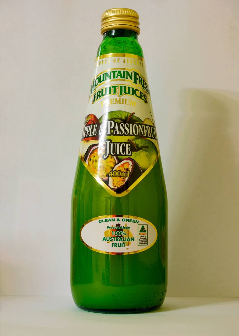 Green glass bottle of fruit juice with a yellow cap and colorful label on a white background