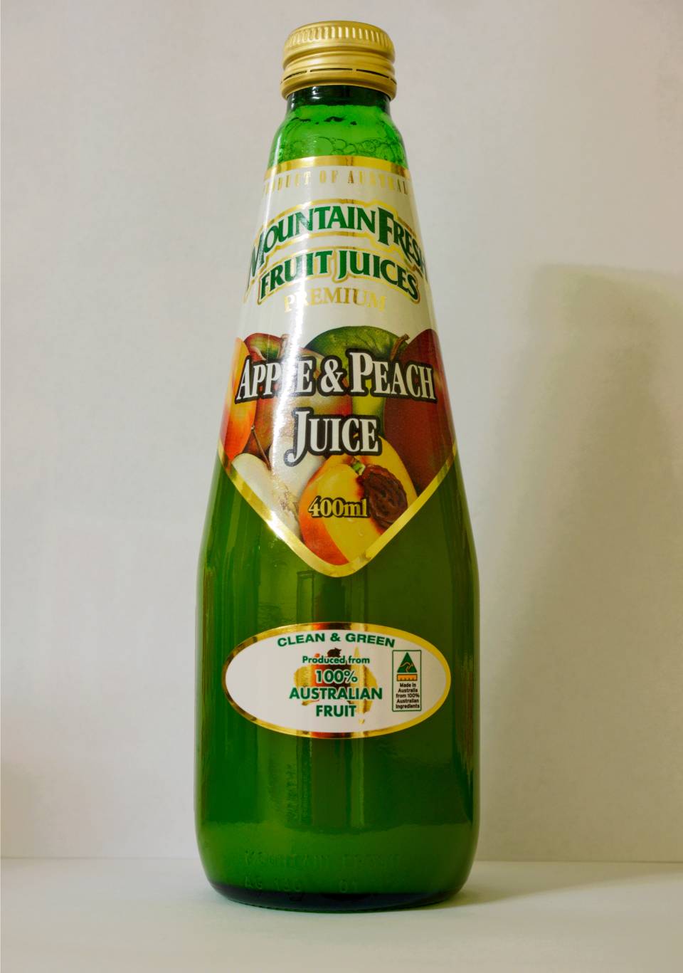 Green glass bottle of peach juice with a gold cap and colorful label on a plain background