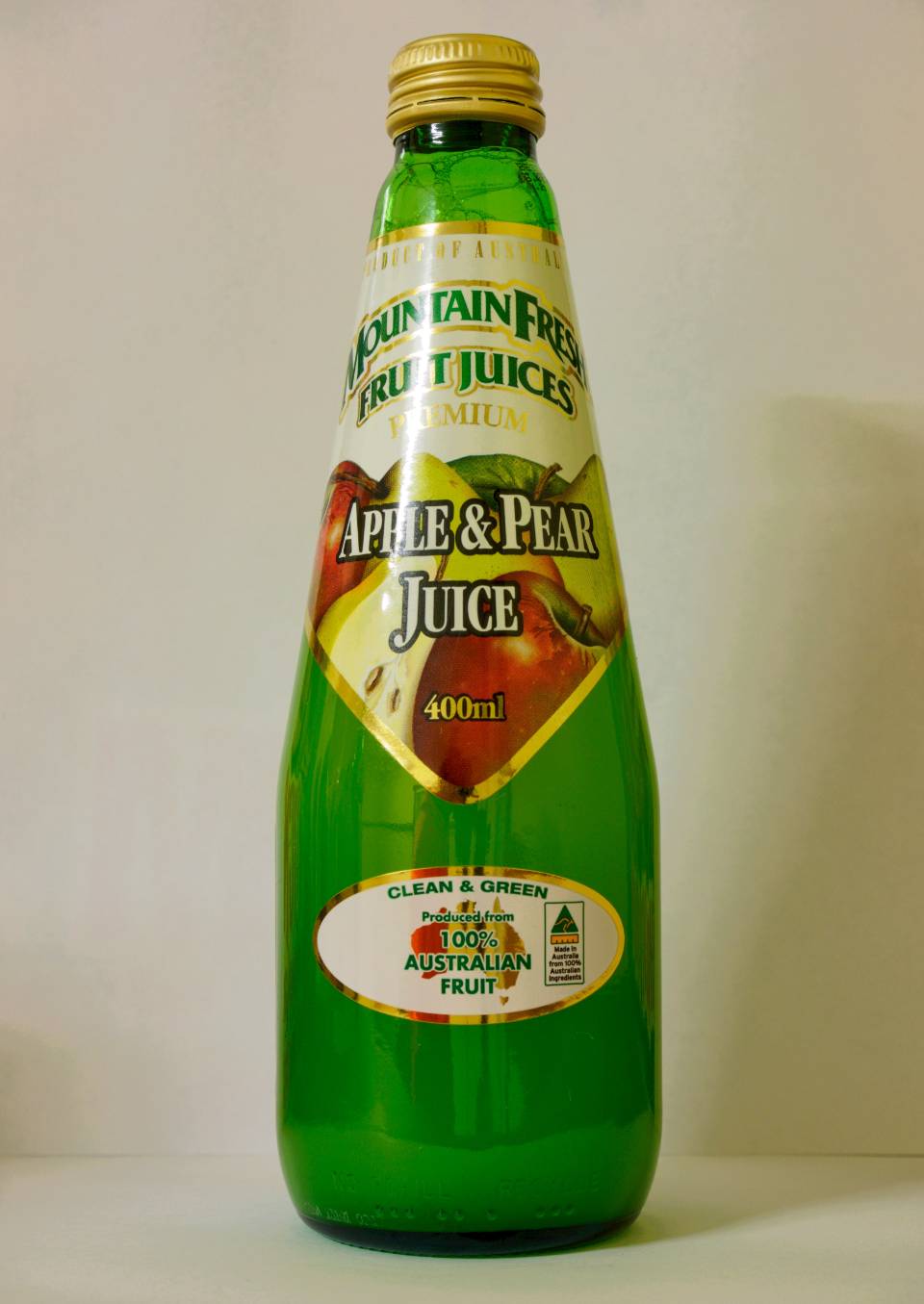Green glass bottle of apple and pear juice with a yellow cap and label on a plain background