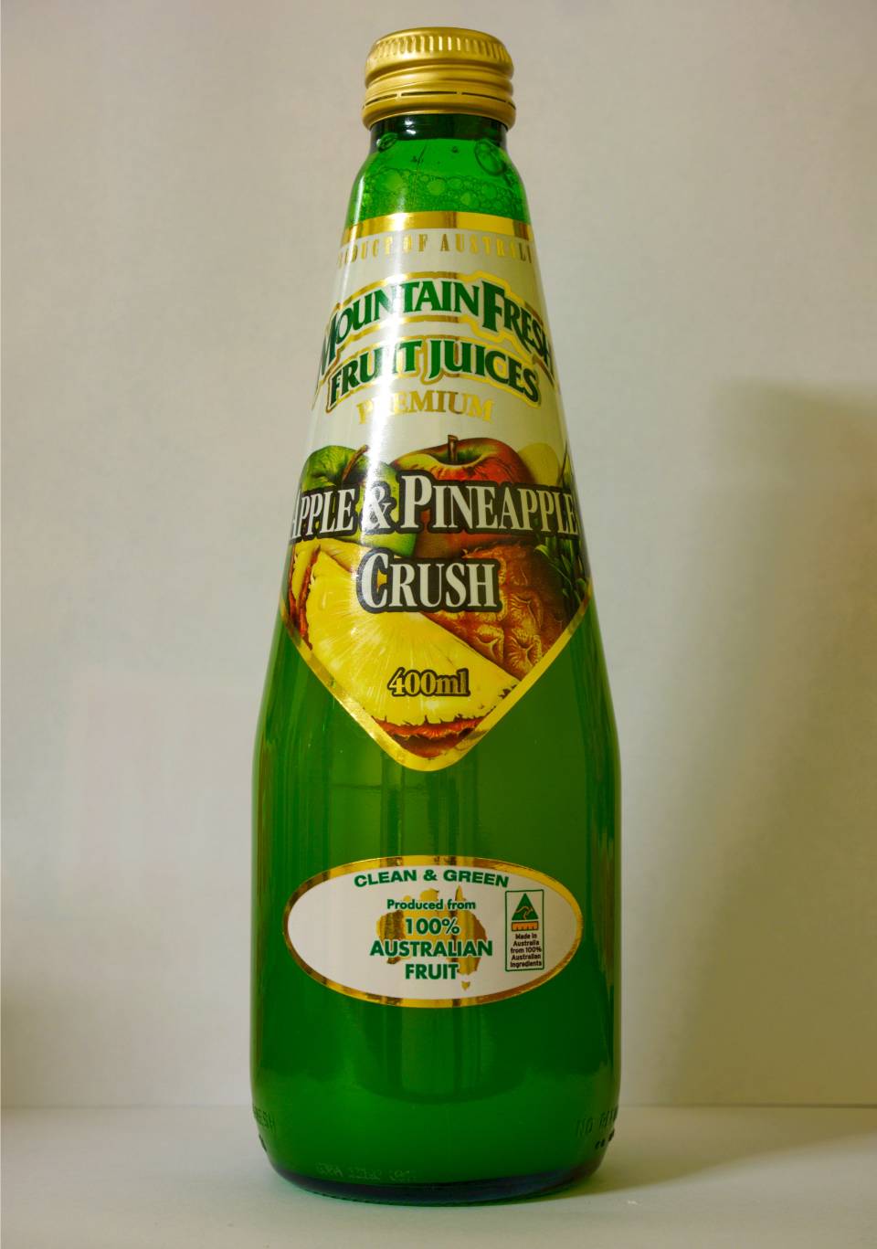 Green bottle of pineapple Crush soda with a gold cap and yellow label on a plain background