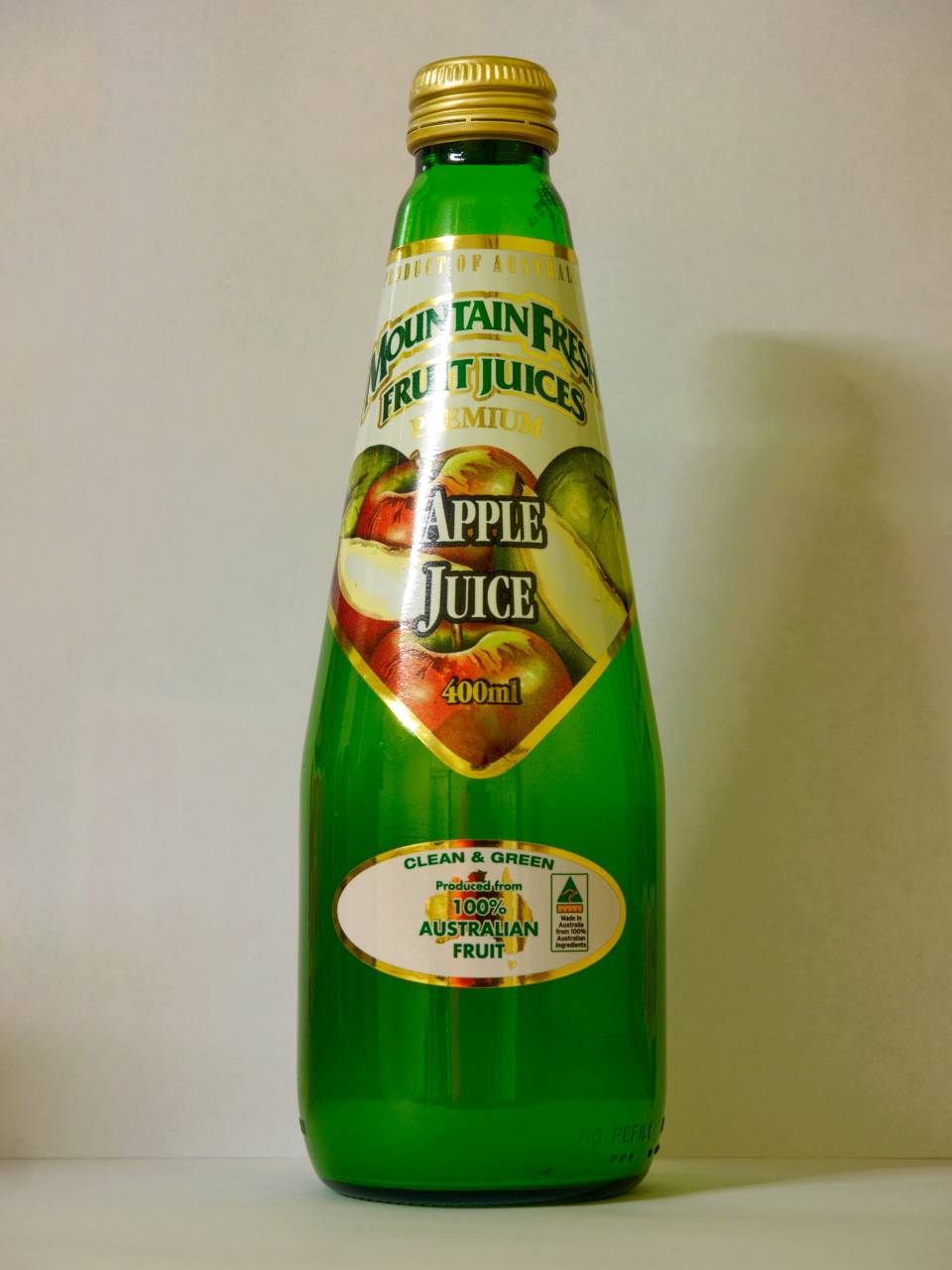 Green glass bottle of apple juice with gold cap and label, standing against a plain white background