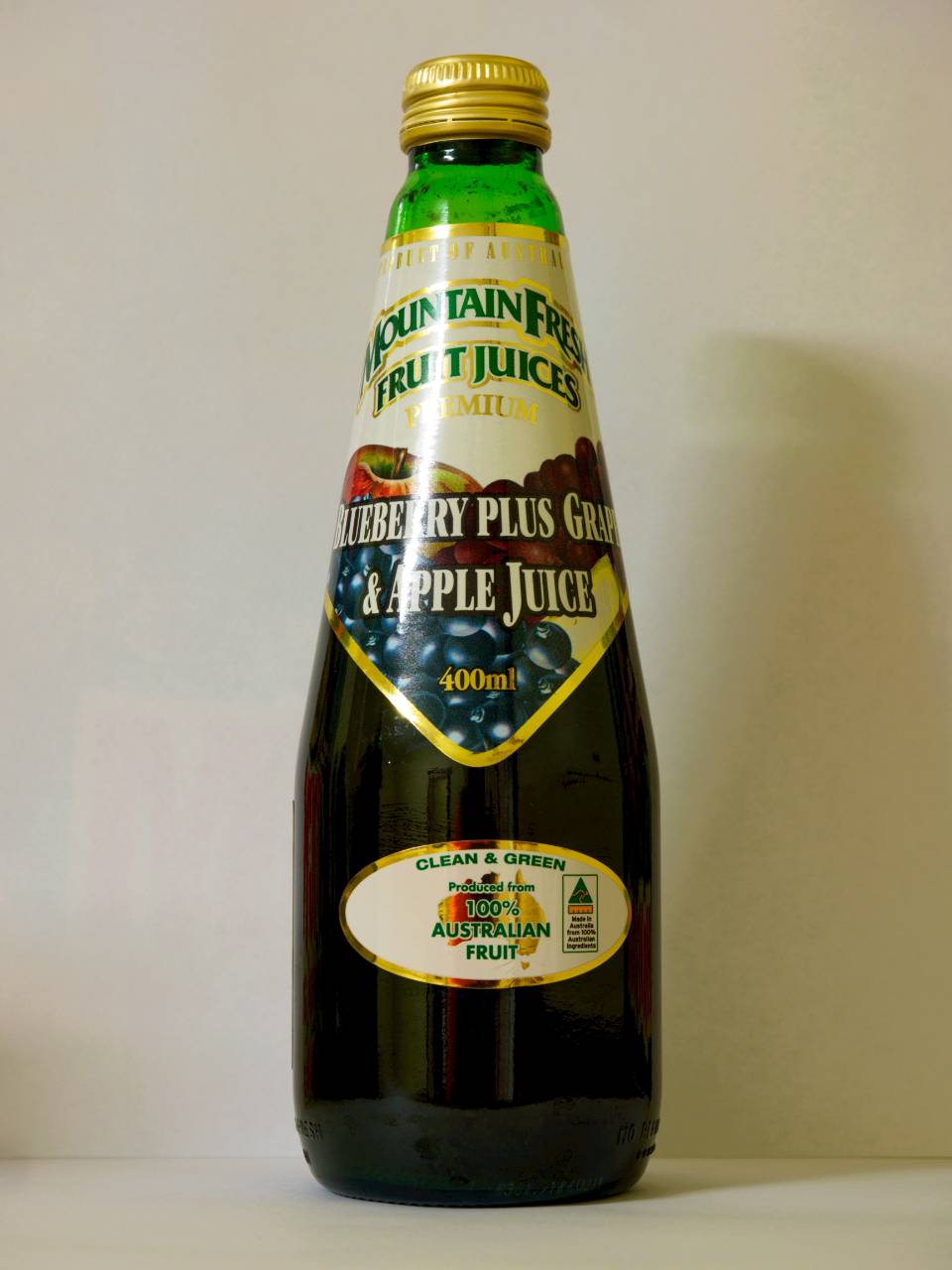 Bottle of green and black fruit juice with gold cap and label on a plain background