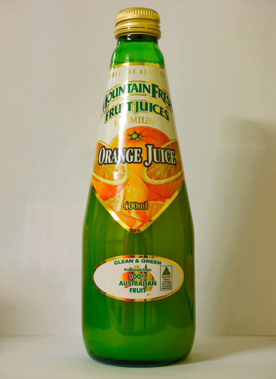 Green glass bottle of orange juice with yellow cap and fruit label, standing upright on a plain background