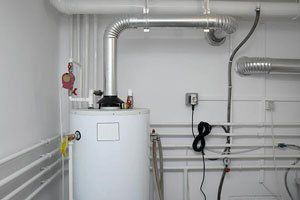 A water heater is sitting in a room next to pipes.