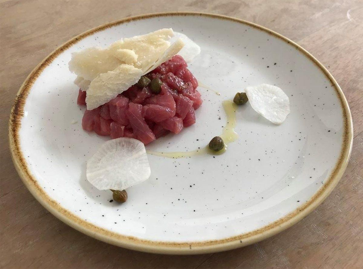 Une assiette blanche garnie de viande et de pain sur une table en bois.
