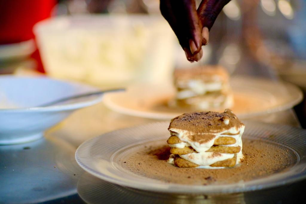 Une personne ajoute du chocolat à un dessert dans une assiette.