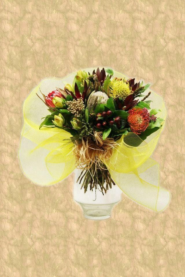 Mazzo di fiori colorati in un vaso, avvolto in una rete gialla, su uno sfondo beige.