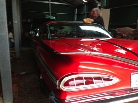 Red classic car being polished inside a garage. A person is washing the car.