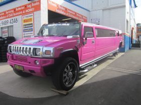 Pink Hummer limousine parked outside an auto shop.