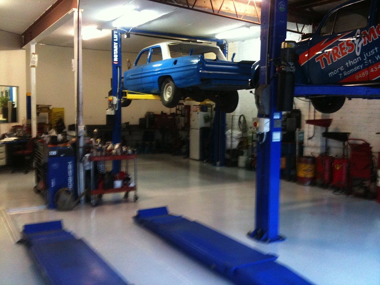 Blue car raised on a lift inside a car repair shop with a shiny gray floor.