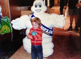 Boy in red striped shirt poses with the Michelin Man mascot, indoors.