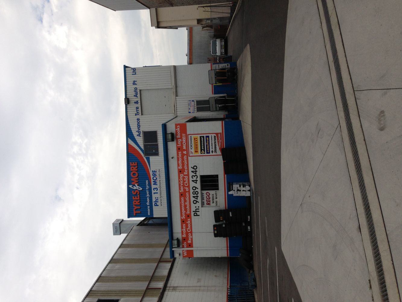 Tire shop building with blue and white colors, sign, and phone number visible. Exterior setting.