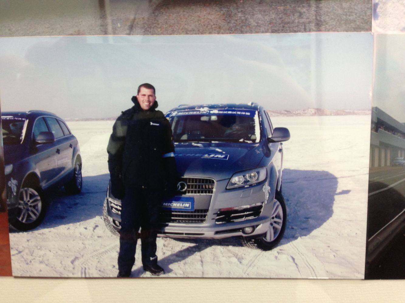 Man standing next to a gray Audi SUV on a snowy plain. Another SUV is visible in the background.