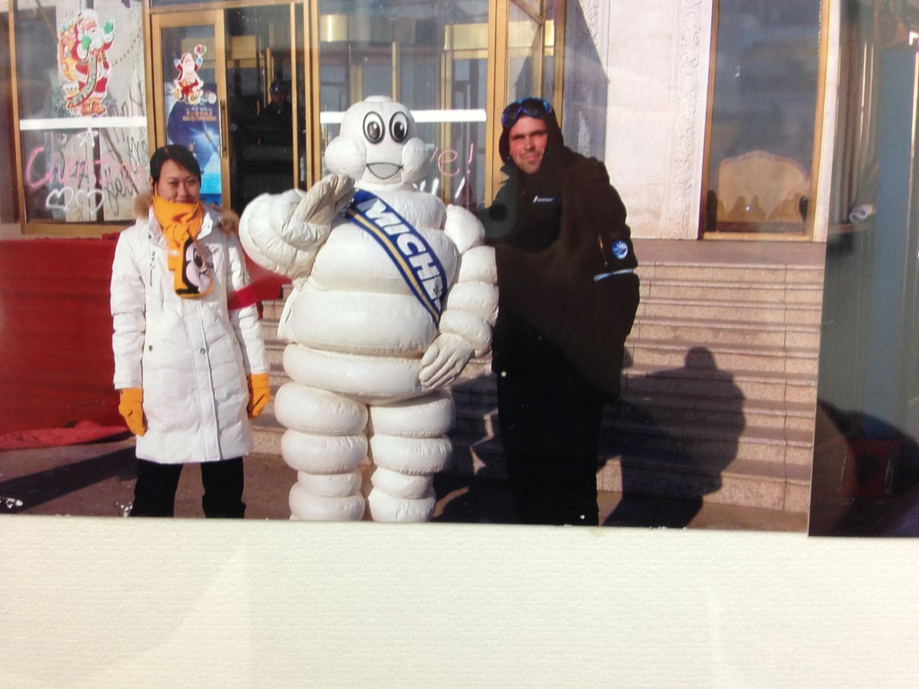 People posing with the Michelin Man in front of a building. The man gives a salute.