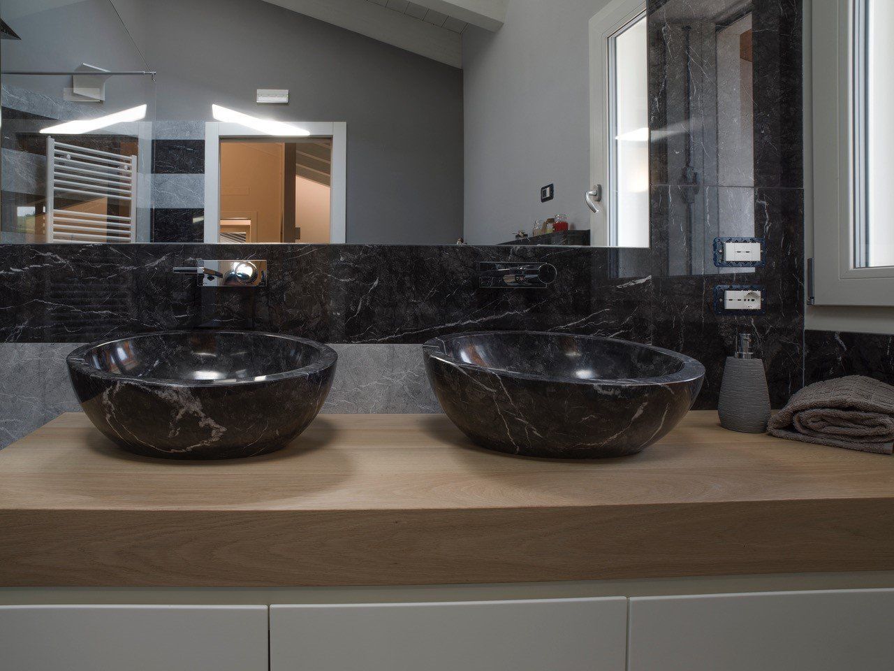 Due lavandini sono appoggiati su un ripiano di legno in un bagno.