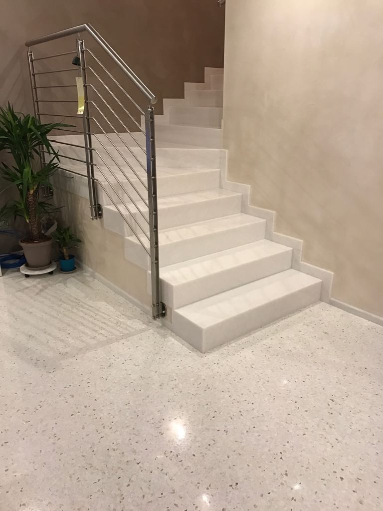 Una scala bianca con una ringhiera in acciaio inossidabile in una stanza.